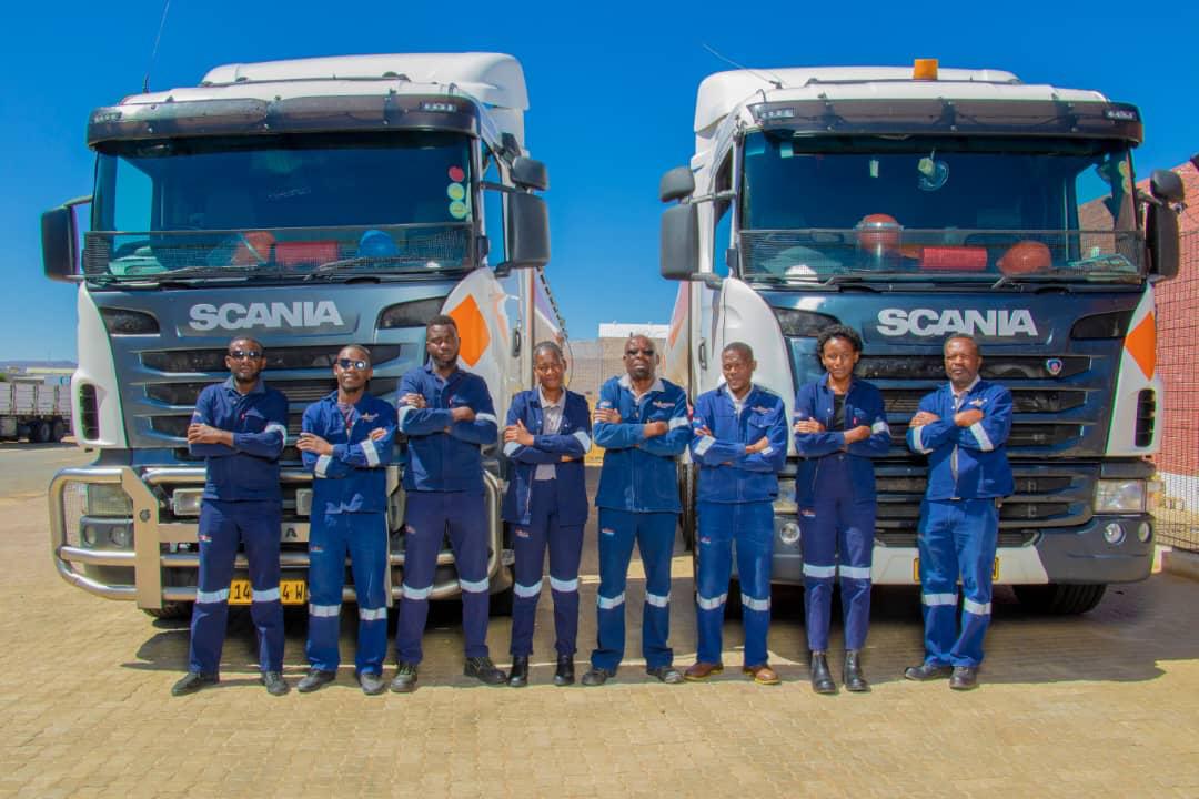 Eight staff with arms crossed standing in front of two trucks